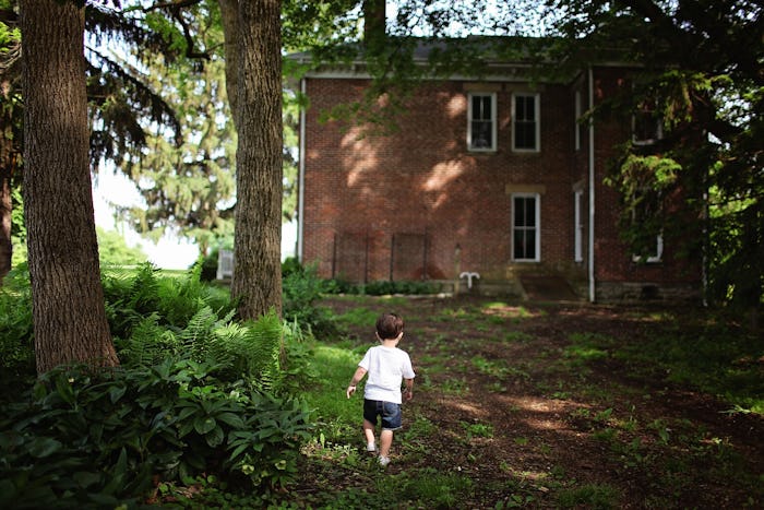 A toddler walking around the front yard of an old house