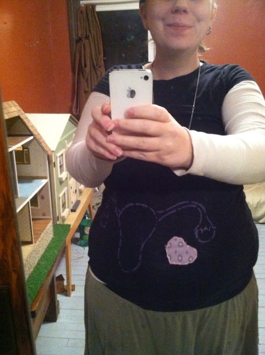 A pregnant woman taking a mirror selfie in a black shirt with an illustrated uterus and a heart