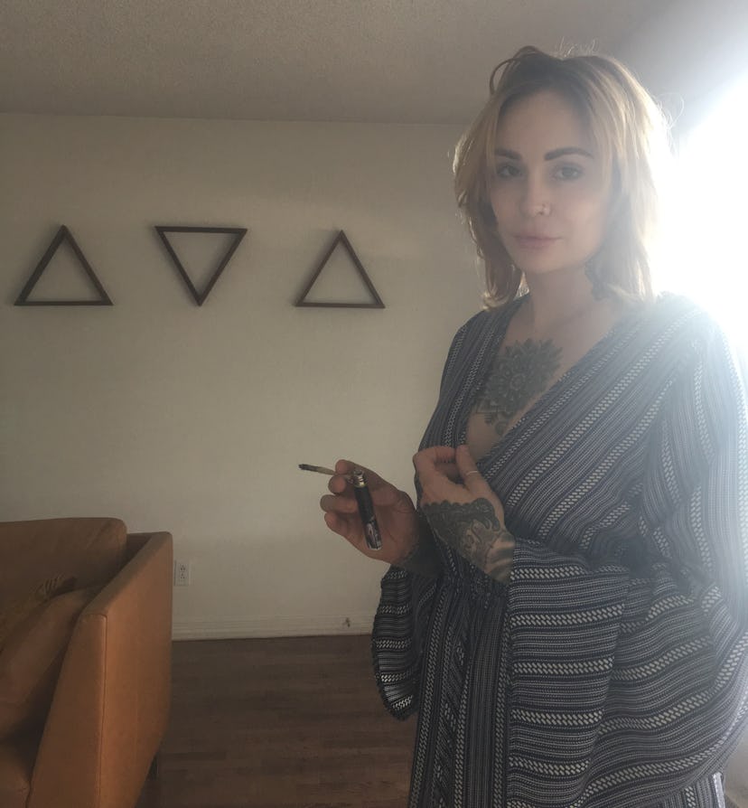 A blonde lady holding a joint while standing in a room