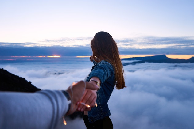 A man holding his girlfriend's hand while she points at the clouds beneath them