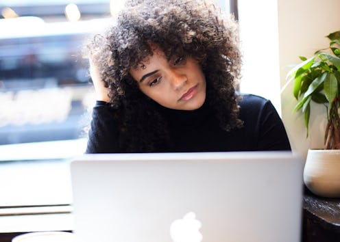 Curly and black-haired girl looking at her laptop screen