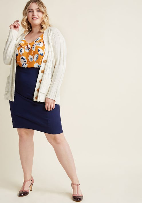 A model wearing a white plus-size grandpa sweater matched with a floral-patterned yellow blouse and ...