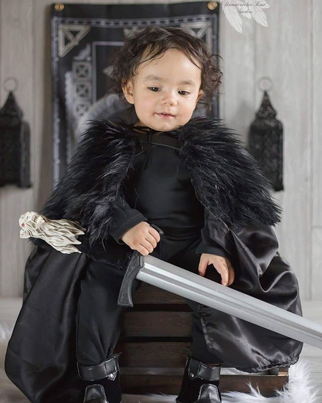 A kid wearing the cool black outfit and having a sword toy in his hand posing for the picture on his...