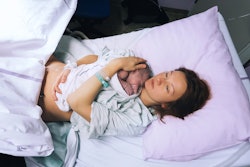 A woman recovering from childbirth lying with her baby in a hospital bed
