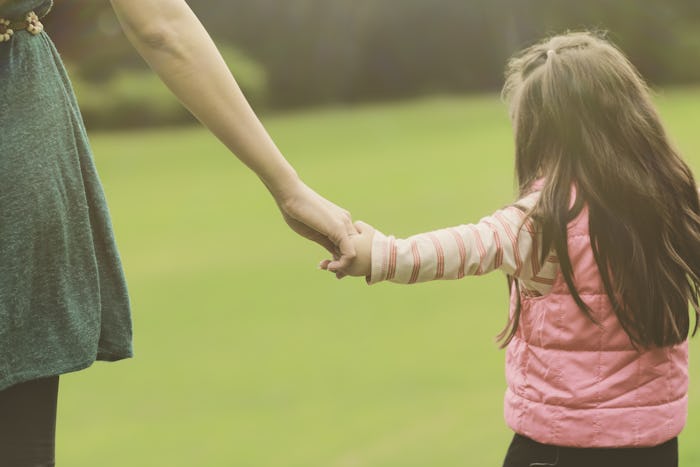 A mom holding her daughters hand while walking through a field