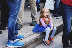 A little girl dressed as Wonder Woman sitting on a curb eating ice cream