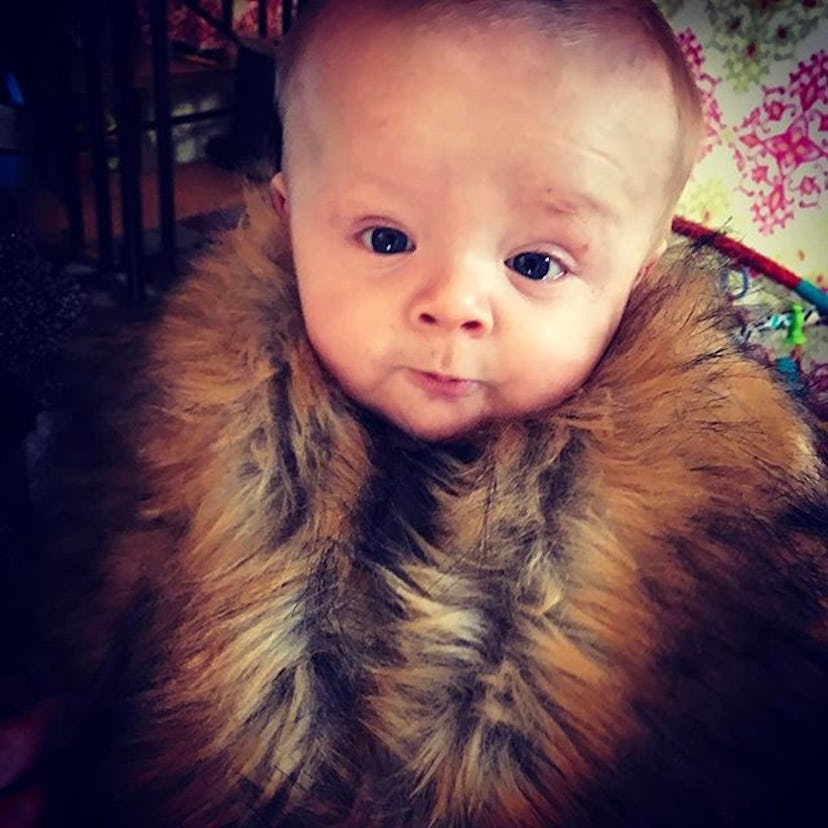 A baby looking straight into the camera and posing for the picture in a fur coat as a true king