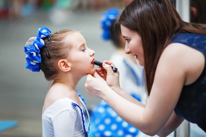 A mom putting lipstick on her young daughter before a dance competition.