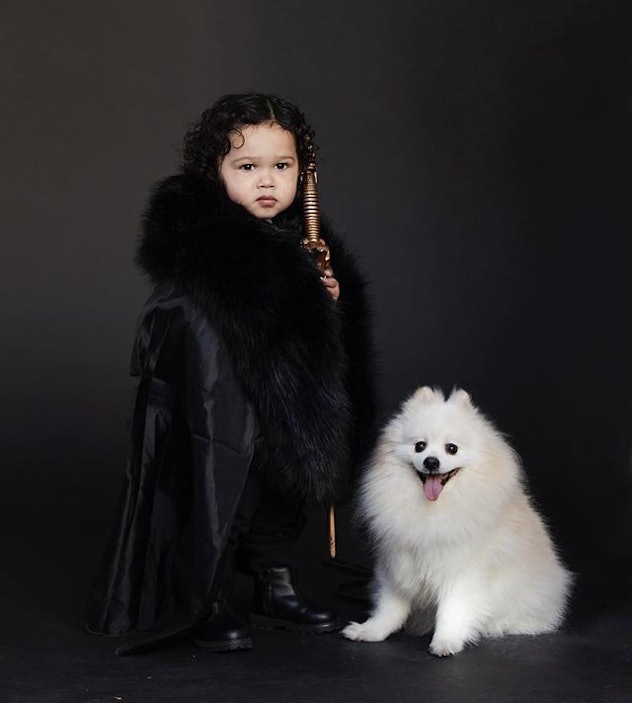 A little kid wearing a black fur coat and posing for the picture with his little white dog