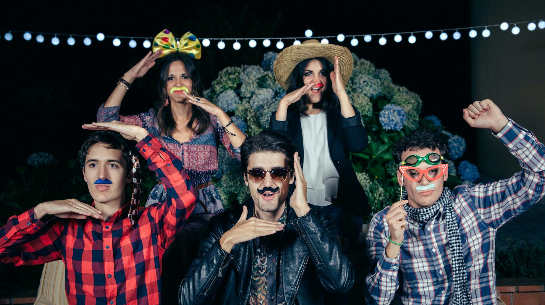 Friends posing for a photo in Halloween costumes with sunglasses, bows, hats and fake mustaches 