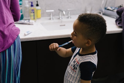 A kid learning to brush his teeth on his own in the bathroom, as his first tooth appears after turni...