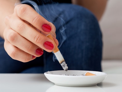 A woman who is trying to conceive, putting out a cigarette in a white ash-tray 