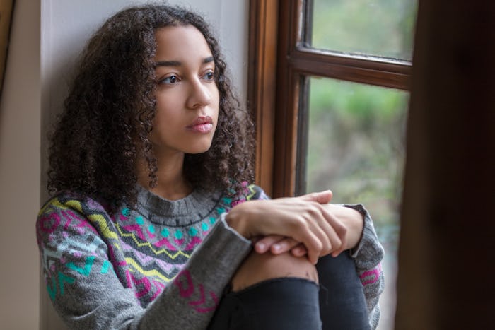 A woman with PCOS sitting on the window sill, looking out pensively 