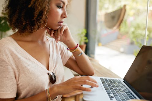 A curly-haired woman sitting with her laptop next to a window while working from home
