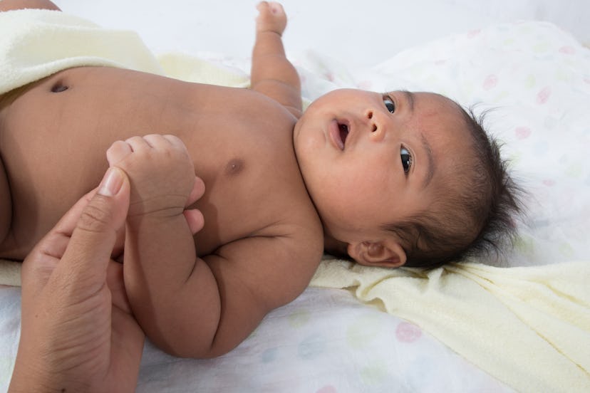 A baby laying on it's back holding it's moms finger