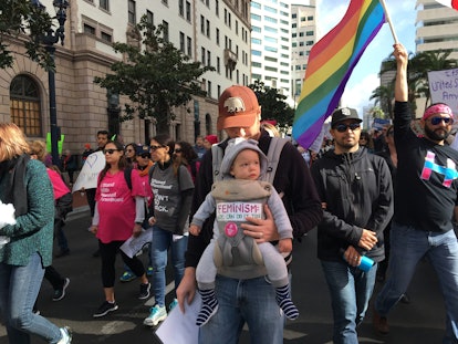 A father walking with his son in a baby carrier at the Women's March