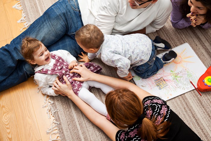 A mother tickling her baby while lying on the floor next to other family members.