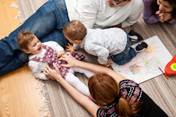 A mother tickling her baby while lying on the floor next to other family members.