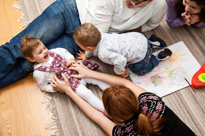 A mother tickling her baby while lying on the floor next to other family members.