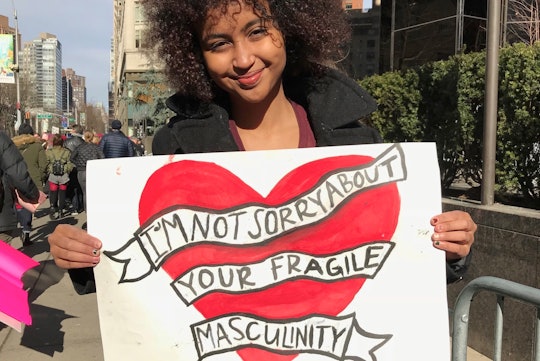 A woman holding a banner with a heart and "I'm not sorry about your fragile masculinity" text