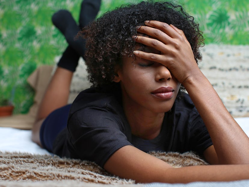 A woman with short curly hair lying on her stomach, covering half of her face with a hand 