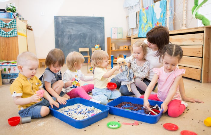 Six kids and their teacher at day care playing with sandboxes on the floor