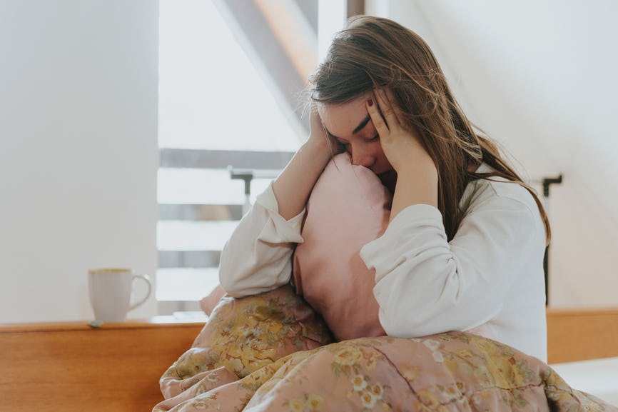 A girl covered with a blanket, holding her head with her hands because of having a flu