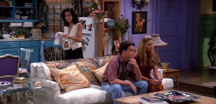 Chandler and Phoebe sitting on the couch while Monica cleans behind them in a Friends episode