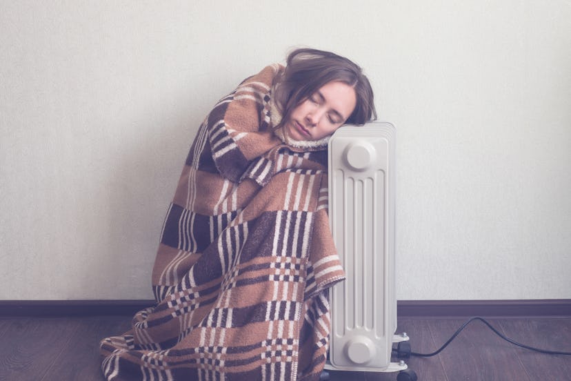 A girl who is cold, covered with a blanket, leaning on the radiator