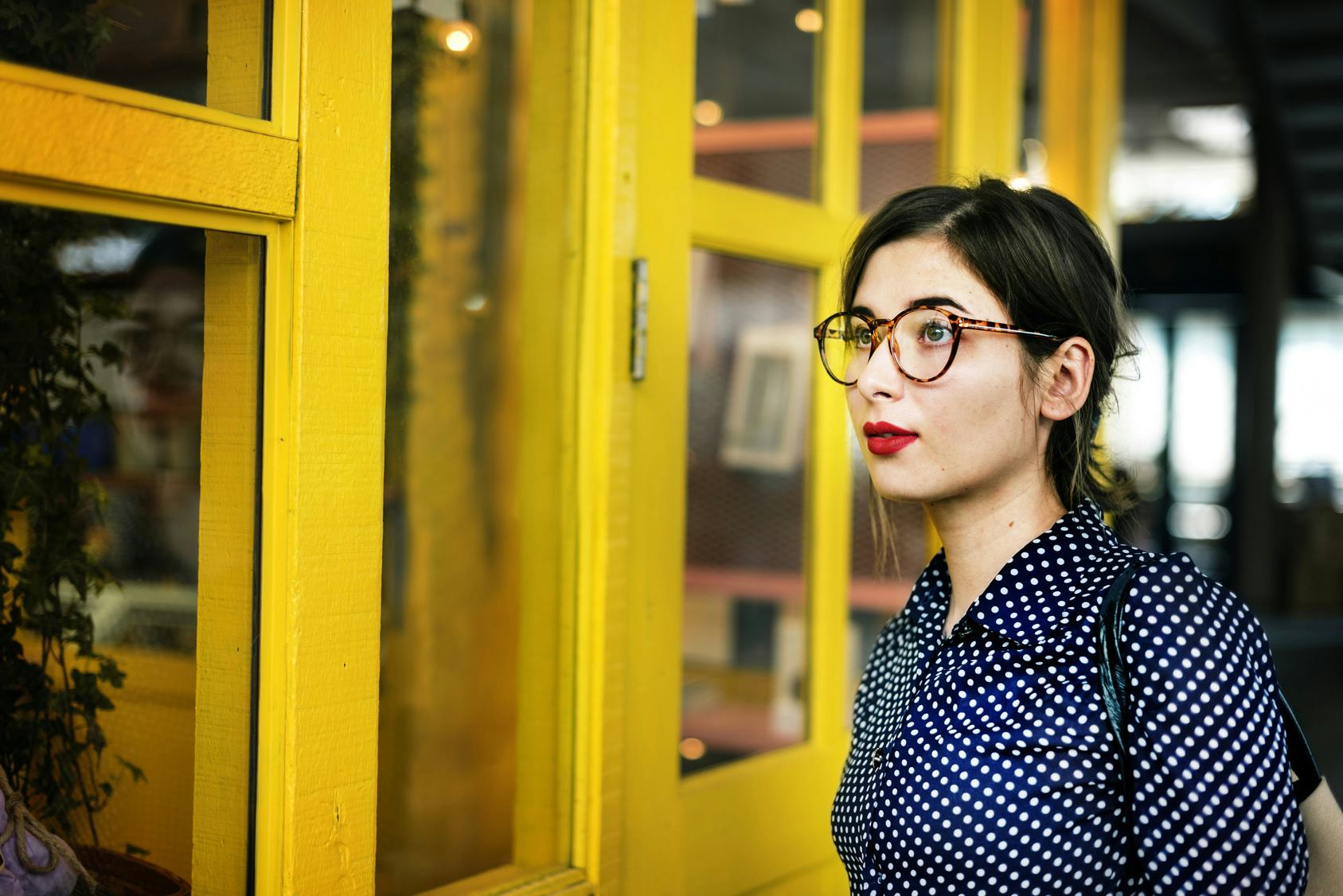 Brunette woman with glasses standing next to a yellow window