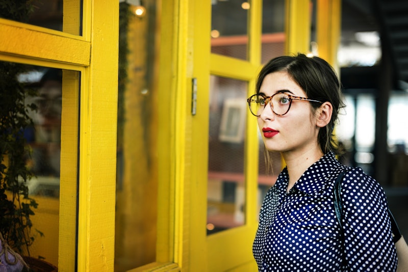 Brunette woman with glasses standing next to a yellow window