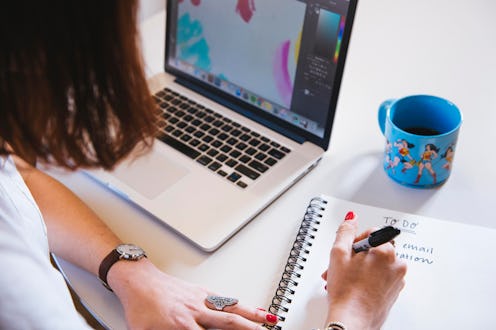 A woman writing down in her notebook and looking at her laptop who is stressed out from worl