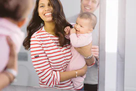 Parents hold their newborn baby and take a mirror selfie while smiling