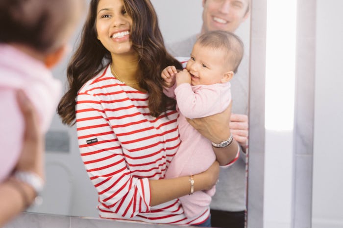 Parents hold their newborn baby and take a mirror selfie while smiling