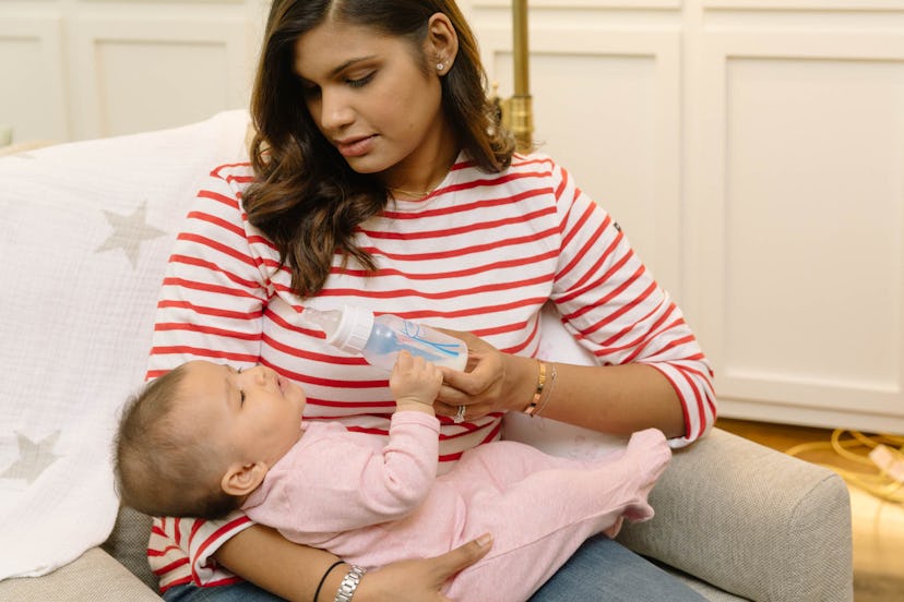 A mom in a striped shirt holding her baby in her lap and bottle feeding it