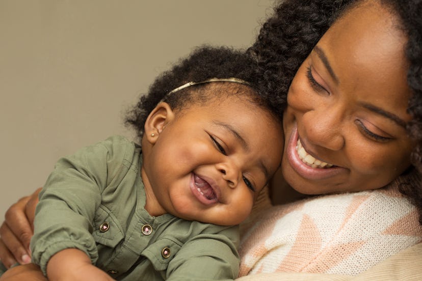 A mom holding her baby close to her while they both look at something and laugh