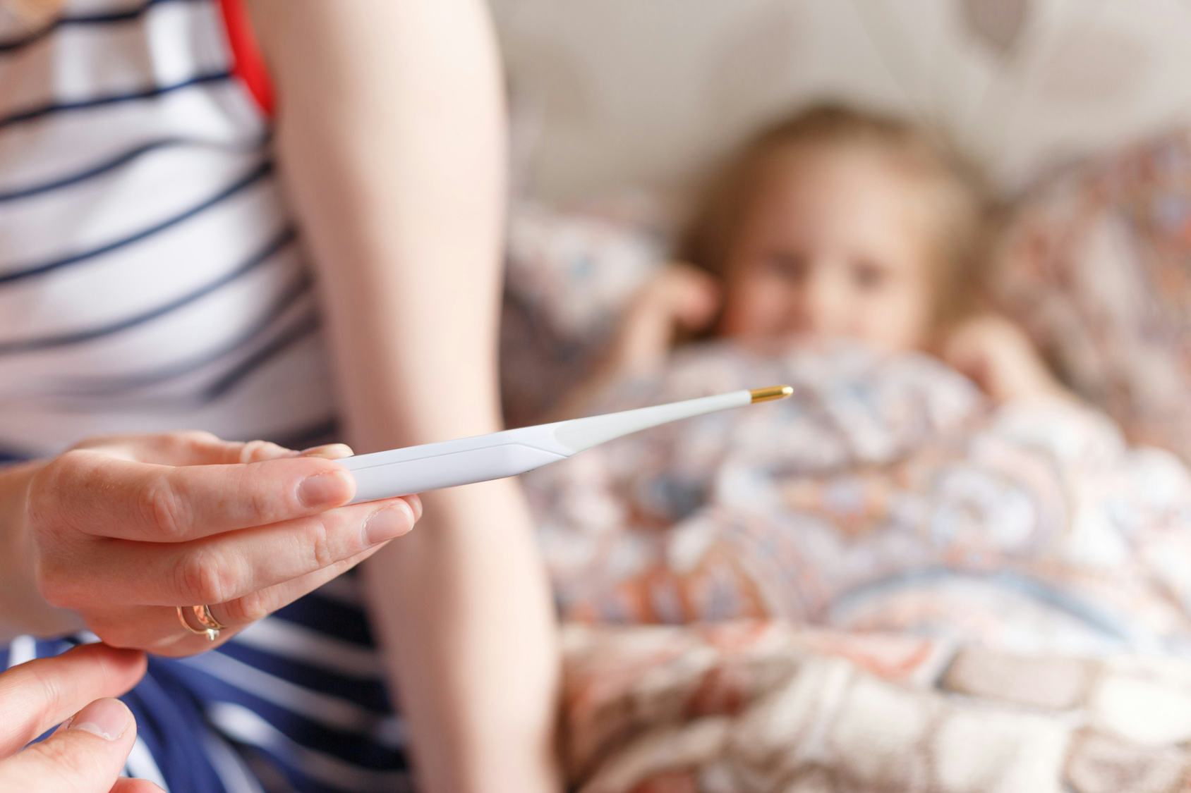 A parent looking a thermometer while sitting next to daughter with flu 