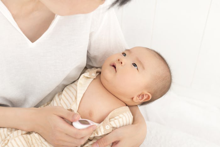 A mother holding an infant and measuring its body temperature due to a fever