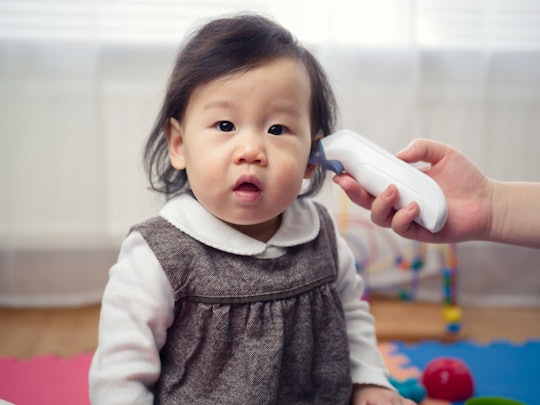 1-year-old with a fever getting her temperature taken via ear thermometer 