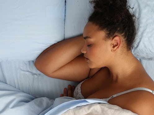 A woman lying in bed in a white bra covered by a blanket and sweating