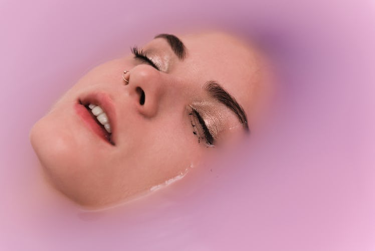 A woman taking a bath in pink water as a self-care ritual with only her face being visible