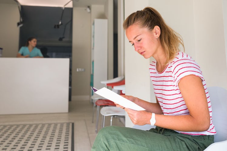 A blonde woman is sitting in the waiting room reading a flyer after getting the flu shot