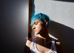 A man with a blue pixie haircut standing against a wall posing for a picture.