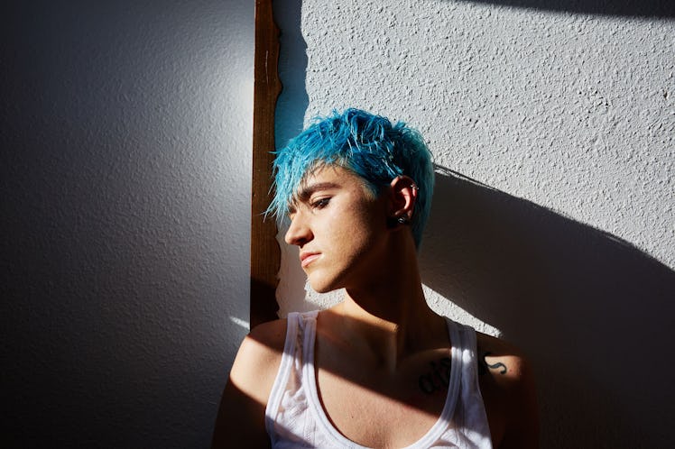 A man with a blue pixie haircut standing against a wall posing for a picture.