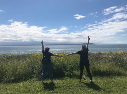 A couple holding hands while standing on top of a hill and looking at the landscape on a sunny day