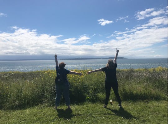 A couple holding hands while standing on top of a hill and looking at the landscape on a sunny day