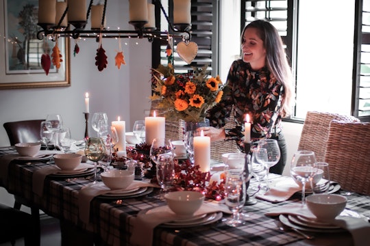 A woman hosting Thanksgiving smiling while decorating a dinner table