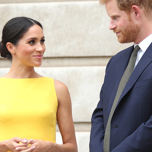 Meghan Markle smiling in a yellow dress while looking at Prince Harry in a navy suit, white shirt, a...
