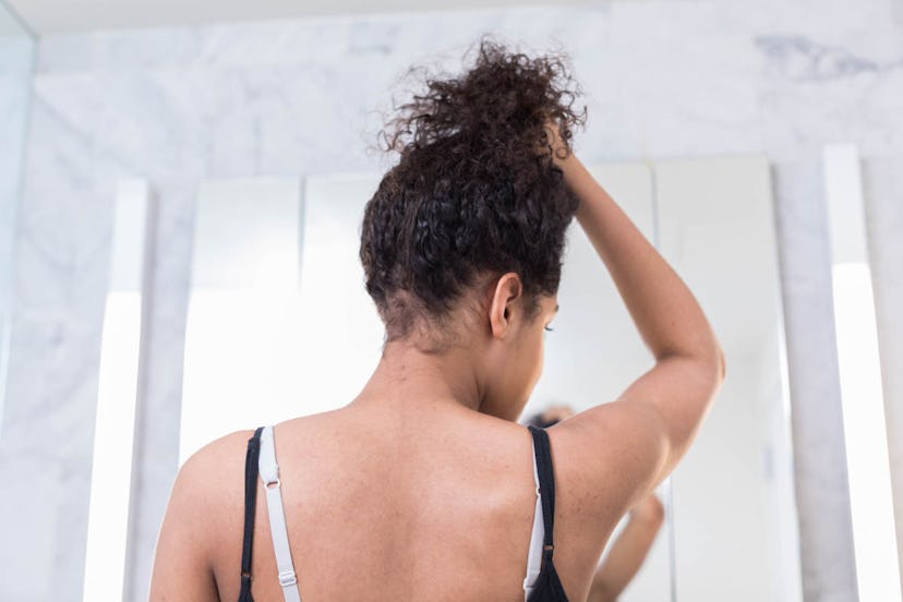 A woman experiencing breast shrinkage looks at herself in the mirror while wearing a black bra and h...