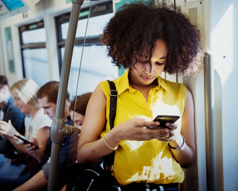 A young woman is seen on a bus, holding her phone.